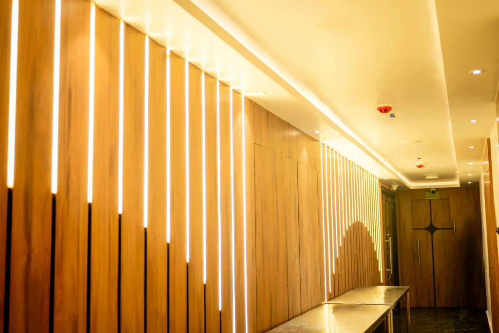 Elegant commercial hallway featuring warm white vertical LED strip lights embedded in natural wood wall panels, creating a sleek, modern ambiance. Energy-efficient LED linear lighting enhances the corridor’s aesthetic and provides soft, even illumination.