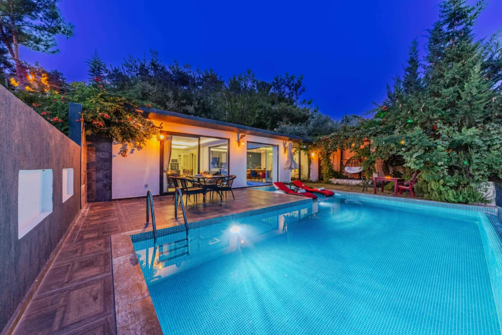 Modern vacation villa with private swimming pool, outdoor dining area, and warm LED strip lighting illuminating the patio and garden at dusk. Energy-efficient LED lights enhance the cozy evening ambiance.