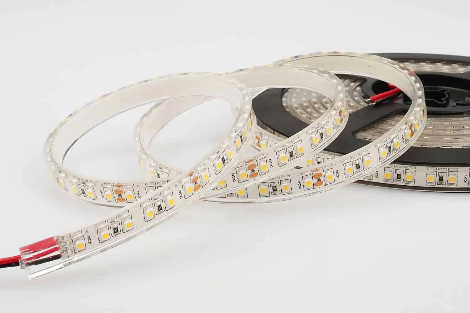 Coiled LED strip light rolls with small yellow LEDs on a white background