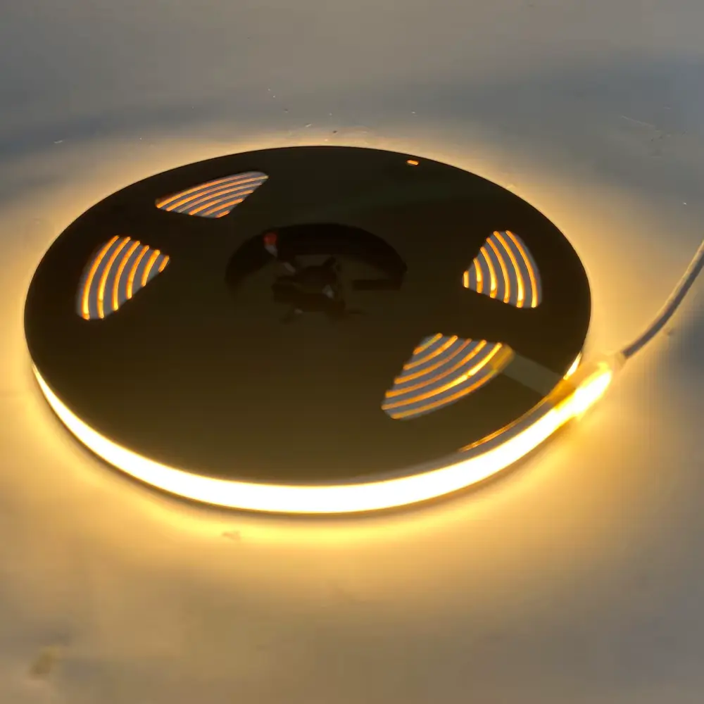 Roll of warm-white LED strip light, glowing along its edge on a dark circular spool kit pieceing laid on a surface.