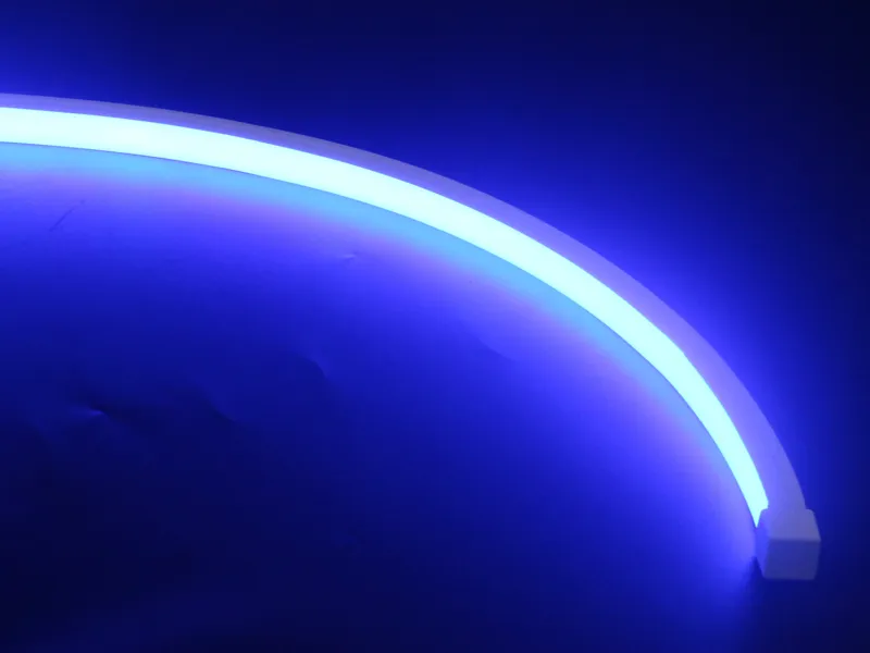 Close-up macro shot of a flexible IP68 blue silicone LED strip light bent in a smooth curve against a deep blue background, showing the uniform light diffusion and flexibility of the full silicone extrusion waterproof encapsulation