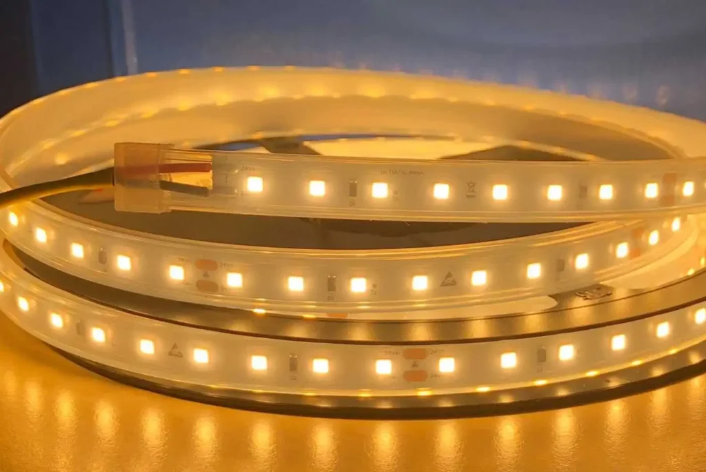 Coiled warm-white LED strip lights with a plug-in connector at one end, glowing softly.