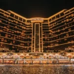 Wynn Palace hotel illuminated at night with a lit fountain pool in front.