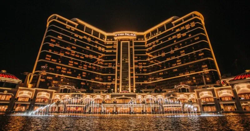 Wynn Palace hotel illuminated at night with a lit fountain pool in front.