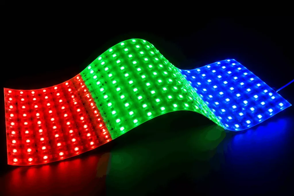 Gięty arkusz elastycznego oświetlenia LED RGB ze zmiennymi kolorami, ułożony w falisty wzór pokazujący czerwone, zielone i niebieskie sekcje, prezentujący panel SMD5050 RGB do kasetonów reklamowych, gablot ekspozycyjnych i wewnętrznego podświetlenia dekoracyjnego.
